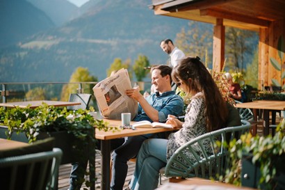 Paar sitzt am Tisch auf der Terrasse, der Mann liest Zeitung