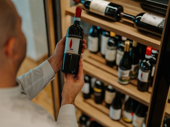 Mann steht vor Weinregal und schaut sich eine Weinflasche genau an